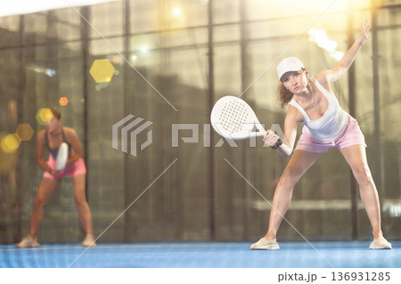 Woman with racket training on outdoor court playing padel game and hitting ball 136931285