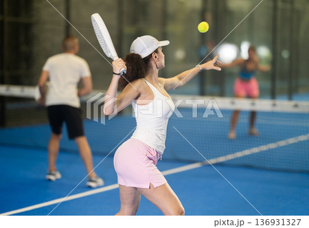 Woman with racket training on outdoor court playing padel game and hitting ball 136931327