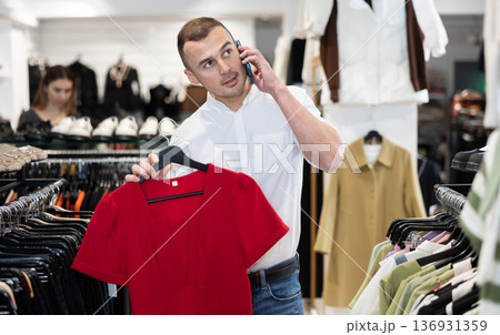 While shopping, man chooses gift, examines womans dress and talks on phone 136931359