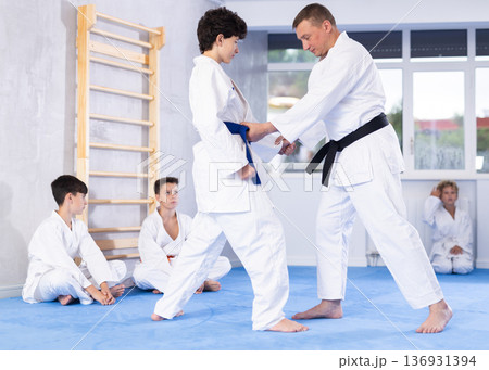 Skilled judo trainer demonstrating wrestling technique on juvenile practitioner 136931394