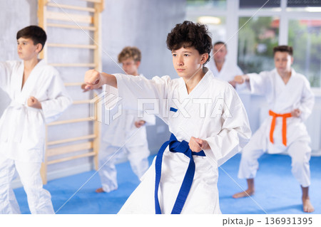 Teenage boy with group of karate practitioners performing kata routines 136931395