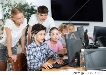 Preteen boys and girls working on computer together with teacher in IT cabinet Preteen boys and girls working on computer together with teacher in IT cabinet 136931406