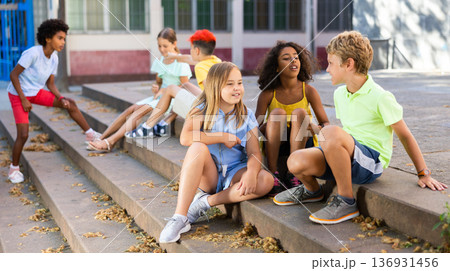 Positive tweenagers friendly blabbing while sitting on steps outdoors 136931456