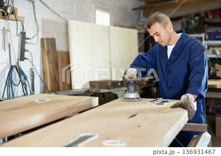 Man sanding a wooden board using sanding machine Man sanding a wooden board using sanding machine 136931467