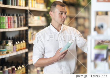 Thoughtful young man purchaser choosing cosmetic product in large supermarket 136931533