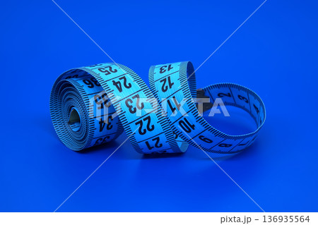 Blue measuring tape coiled against a solid blue background, symbolizing measurement and precision 136935564