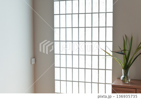 Glass block window natural light minimalist interior wooden cabinet green plant modern home clean wall bright room simple decor peaceful atmosphere 136935735