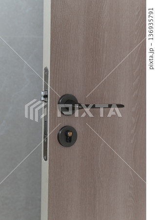 Modern wooden door with black metal handle lock and keyhole partially open minimalist interior neutral color palette contemporary home security privacy concept Modern wooden door with black metal handle lock and keyhole partially open minimalist interior neutral color palette contemporary home security privacy concept 136935791