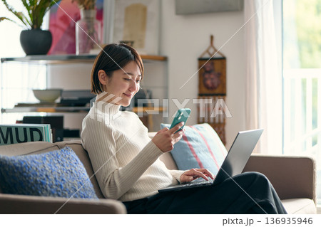 パソコンを操作しながらスマートフォンを手に持つ女性 136935946