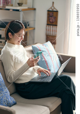 パソコンを操作しながらスマートフォンを手に持つ女性 136935950