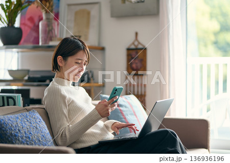 スマートフォンを操作しながら不安な表情をする女性 スマートフォンを操作しながら不安な表情をする女性 136936196