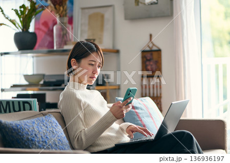 スマートフォンを操作しながら不安な表情をする女性 スマートフォンを操作しながら不安な表情をする女性 136936197