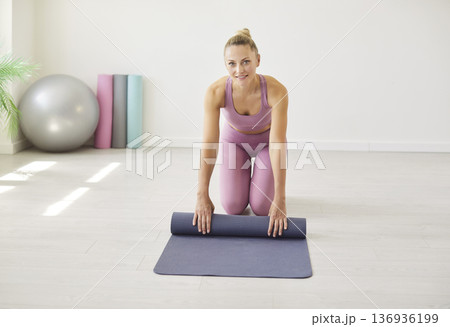 Fit woman unrolling grey yoga mat on floor before start of training in gym, preparation for workout Fit woman unrolling grey yoga mat on floor before start of training in gym, preparation for workout 136936199