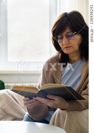 Woman wearing glasses reading book at home 136936241