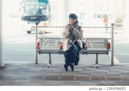 バス停で座ってスマートフォンを見る冬の女性 136936685