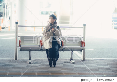 バス停で座ってスマートフォンを見る冬の女性 136936687
