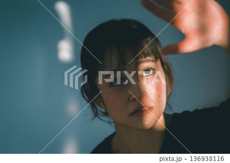 窓から射し込む光を手で遮る若い女性 136938116
