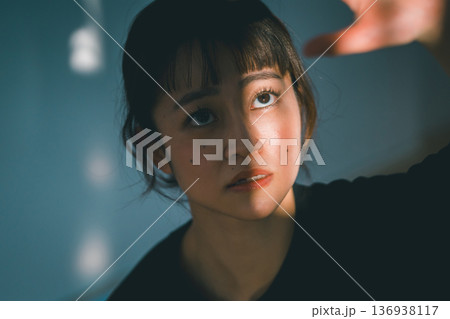 窓から射し込む光を手で遮る若い女性 窓から射し込む光を手で遮る若い女性 136938117