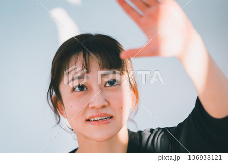 太陽の光を手で遮る笑顔の女性 136938121