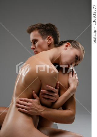 Intimate artistic portrait of a sensual nude couple embracing on a gray background. Intimate artistic portrait of a sensual nude couple embracing on a gray background. 136938377