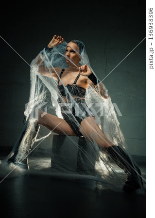 Powerful woman in black lingerie and boots trapped in a giant spiderweb against a dark background. Powerful woman in black lingerie and boots trapped in a giant spiderweb against a dark background. 136938396