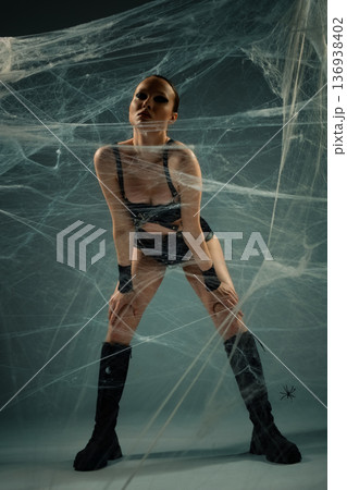 Powerful woman in a black leather outfit and boots, entangled in a large spiderweb. Powerful woman in a black leather outfit and boots, entangled in a large spiderweb. 136938402