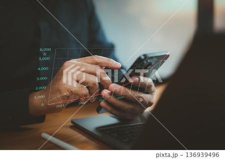 Businessman Analyzing Growth Charts on Smartphone with Laptop in Workspace Businessman Analyzing Growth Charts on Smartphone with Laptop in Workspace 136939496