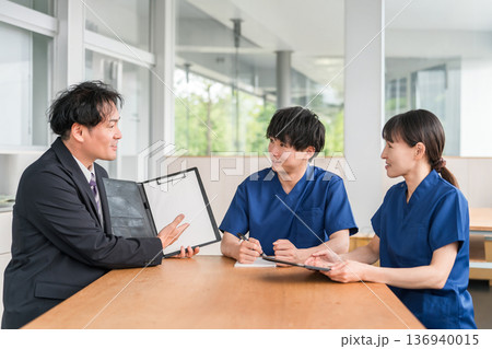 営業,商談する医療機器メーカーの男性ビジネスマンとスクラブ姿の医療従事者の男女 営業,商談する医療機器メーカーの男性ビジネスマンとスクラブ姿の医療従事者の男女 136940015