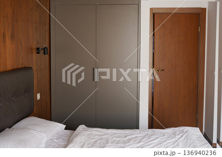Modern cozy bedroom interior with wardrobe wooden door and soft lighting Modern cozy bedroom interior with wardrobe wooden door and soft lighting 136940236