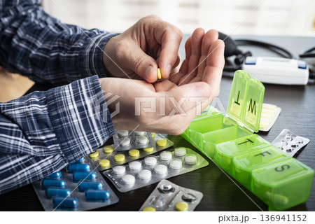 Middle aged caucasian man counts out pills for distributing scheduled dose of medication into pillbox Middle aged caucasian man counts out pills for distributing scheduled dose of medication into pillbox 136941152