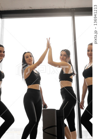 A group of women in athletic wear celebrate their fitness achievement with a high five, embodying teamwork and success A group of women in athletic wear celebrate their fitness achievement with a high five, embodying teamwork and success 136941213
