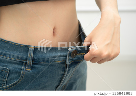 Young Asian woman losing weight wearing loose pants in oversize jeans. 136941993
