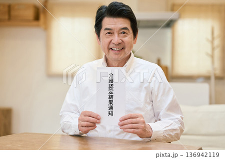 笑顔で介護認定通知書を持つアジア人シニア男性 136942119