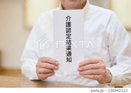 笑顔で介護認定通知書を持つアジア人シニア男性 136942122