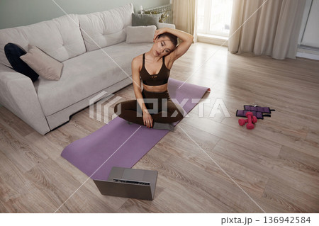 Woman practicing yoga at home on a purple mat in the living room while following an online video lesson during the afternoon Woman practicing yoga at home on a purple mat in the living room while following an online video lesson during the afternoon 136942584