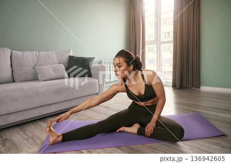 Stretching and improving flexibility in a cozy living room setting during an afternoon yoga session Stretching and improving flexibility in a cozy living room setting during an afternoon yoga session 136942605