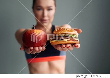 Showing food choices between an apple and a burger while standing in a gym setting Showing food choices between an apple and a burger while standing in a gym setting 136942658
