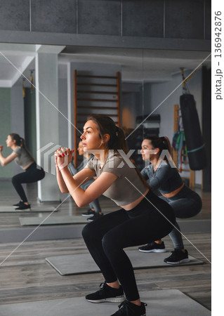 Women training in a gym while performing squats during a fitness session for a healthy lifestyle Women training in a gym while performing squats during a fitness session for a healthy lifestyle 136942876