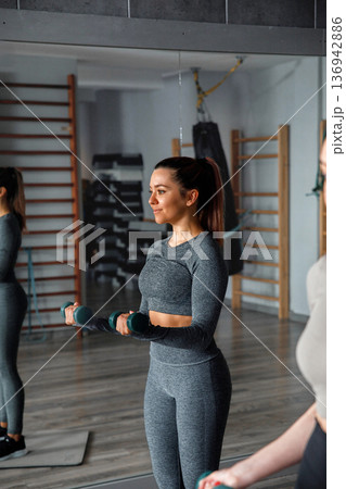 Woman works out with dumbbells in gym during fitness training session in the morning Woman works out with dumbbells in gym during fitness training session in the morning 136942886