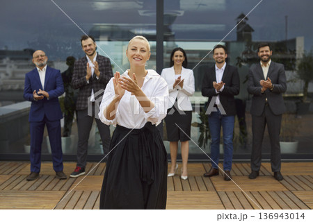 Smiling businesswoman applauding while colleagues clap on rooftop terrace Smiling businesswoman applauding while colleagues clap on rooftop terrace 136943014
