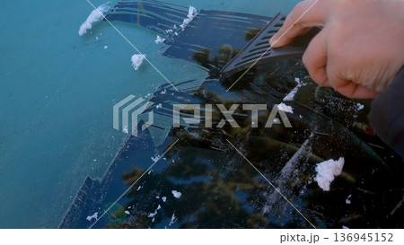 An unidentified hand cleans the car window from ice.  136945152