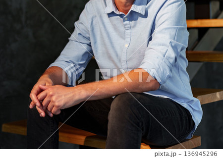 Man sits on wooden stairs with hands clasped in a relaxed pose during evening time Man sits on wooden stairs with hands clasped in a relaxed pose during evening time 136945296