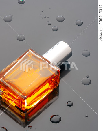 Bottle of orange liquid on dark surface with water droplets around it 136945319