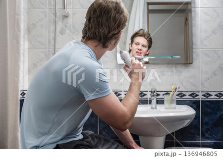 Young man brushing teeth in bathroom mirror in morning routine 136946805