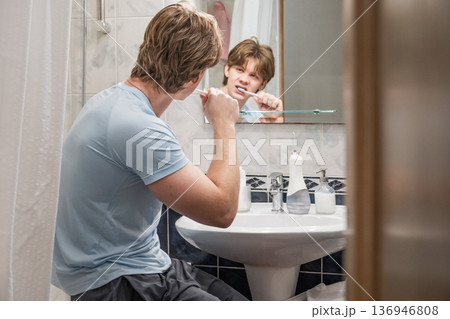 Man brushing teeth sitting near bathroom sink Man brushing teeth sitting near bathroom sink 136946808