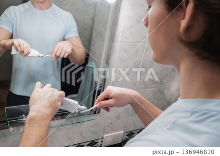 Man applying toothpaste on toothbrush in bathroom mirror Man applying toothpaste on toothbrush in bathroom mirror 136946810