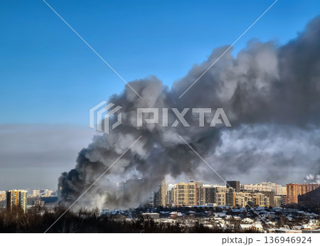 Fire causes thick smoke over city buildings during daytime in urban area 136946924