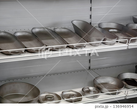 Metal baking pans and trays on the shelves in a kitchen storage area with various sizes and shapes present during the daylight 136946954