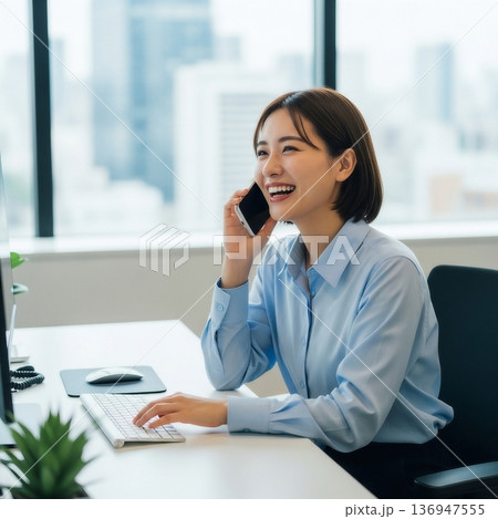 オフィスの中で笑顔でスマートフォンを使って話す若い女性社員 136947555