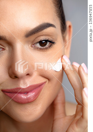 Beauty Woman face skin care. Beautiful close up portrait of a young woman with a glowing skin is applying a skincare product. Cream smear Beauty Woman face skin care. Beautiful close up portrait of a young woman with a glowing skin is applying a skincare product. Cream smear 136947855